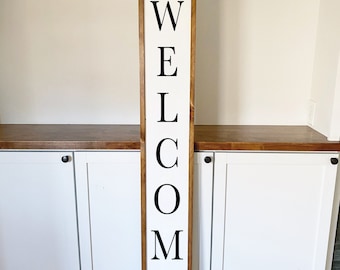 May include: A vertical wooden sign with the word "WELCOME" spelled out in black letters on a white background.