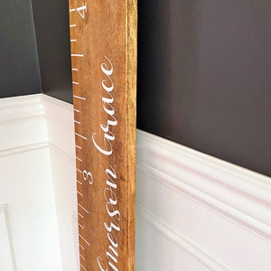 May include: A wooden growth chart with a ruler and the name "Emerson Grace" written in white cursive lettering.