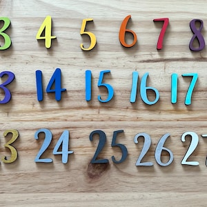 May include: A set of colorful wooden numbers from 1 to 29. The numbers are arranged in three rows, with each row containing ten numbers. The numbers are painted in various colors, including blue, green, yellow, orange, red, purple, pink, and black.