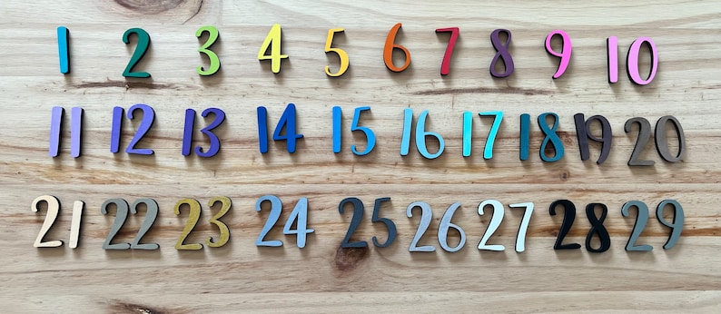 May include: A set of colorful wooden numbers from 1 to 29. The numbers are arranged in three rows, with each row containing ten numbers. The numbers are painted in various colors, including blue, green, yellow, orange, red, purple, pink, and black.