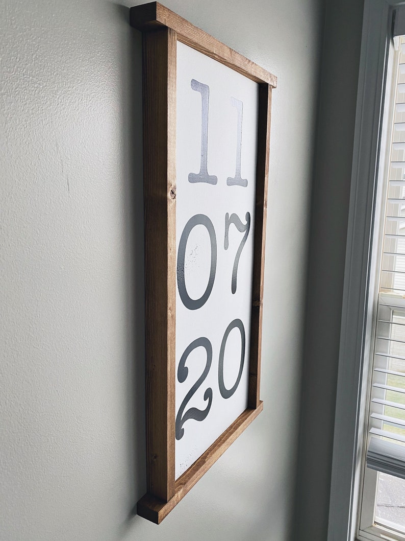 K&ouml;nnte beinhalten: Ein gerahmtes Holzschild mit dem Datum "11 07 20" in Schwarz auf wei&szlig;em Hintergrund.