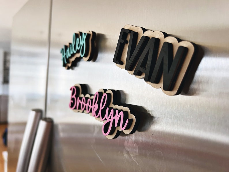 May include: Four wooden name magnets with black outlines and colorful lettering. The names are Hailey in teal, Evan in black, Brooklyn in pink, and a fourth name that is not visible in the image.