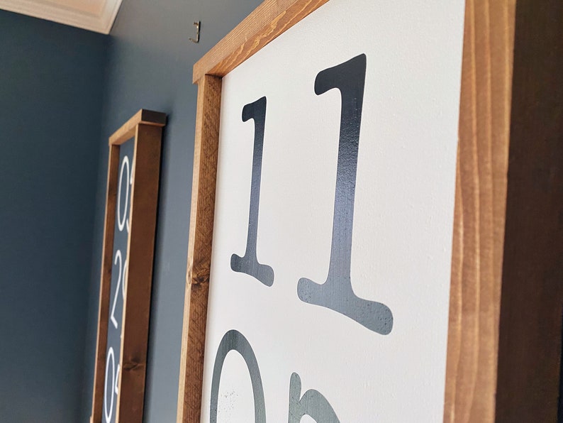 K&ouml;nnte beinhalten: Nahaufnahme eines Holzschildes mit der Nummer "11" in schwarzer Schrift auf wei&szlig;em Hintergrund. Das Schild h&auml;ngt an einer Wand.
