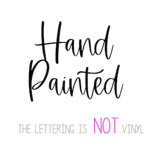 May include: Hand painted sign with the text "Hand Painted" in black cursive lettering. The text "THE LETTERING IS NOT VINYL" is written in white below the main text with the word "NOT" in pink.