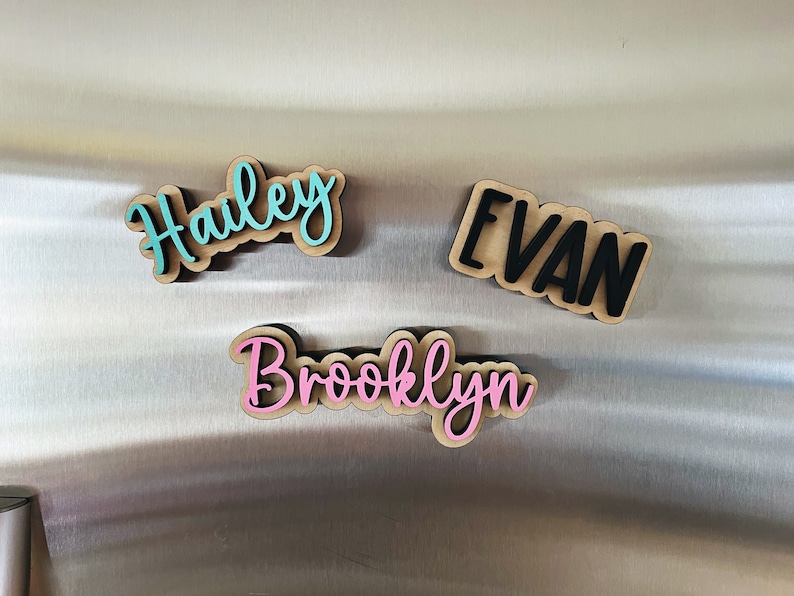 May include: Three wooden name plaques with the names "Hailey", "Evan", and "Brooklyn" written in cursive. The names are painted in different colors: Hailey is turquoise, Evan is black, and Brooklyn is pink.