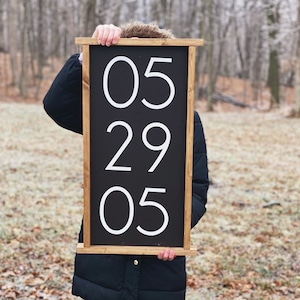 K&ouml;nnte beinhalten: Ein schwarzes Holzschild mit wei&szlig;en Zahlen, die "05 29 05" auf einem schwarzen Hintergrund anzeigen.