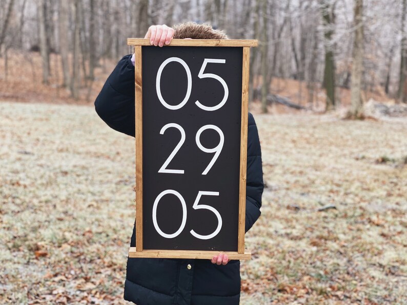 K&ouml;nnte beinhalten: Ein schwarzes Holzschild mit wei&szlig;en Zahlen, die "05 29 05" auf einem schwarzen Hintergrund anzeigen.