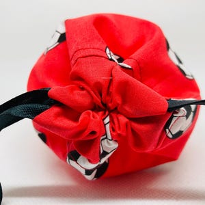 Op de afbeelding: Een rode trekkoordtas met een zwart trekkoord en een patroon van witte en zwarte voetballen.