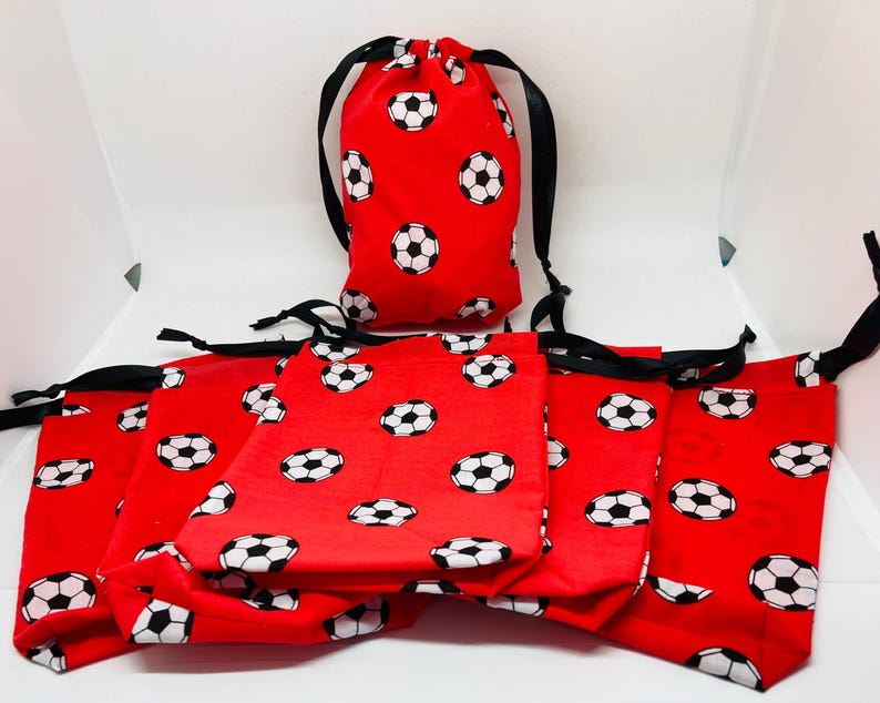Op de afbeelding: Set van acht rode trekzakjes met zwarte trekkoorden. De zakjes zijn versierd met een wit voetbalpatroon.