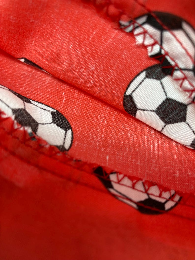 Op de afbeelding: Rode stof met een patroon van witte en zwarte voetballen. De stof is dubbelgevouwen en de naden zijn zichtbaar.