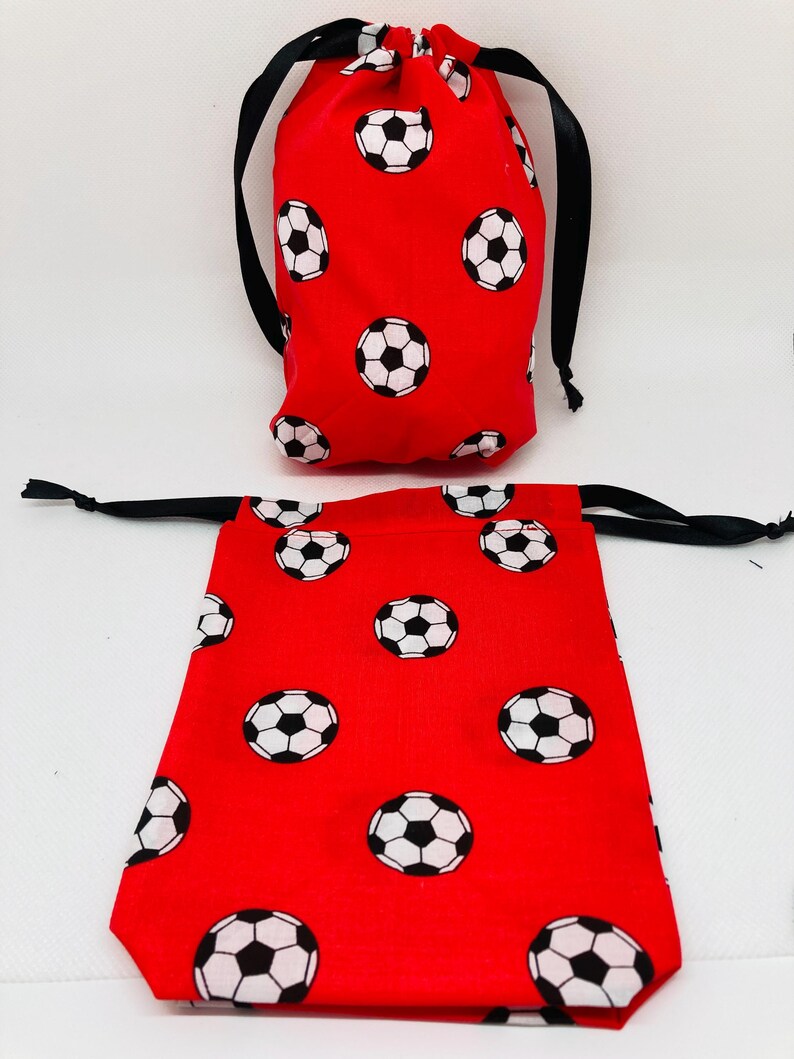 Op de afbeelding: Twee rode trekkoordtassen met een wit voetbalpatroon. De kleinere tas staat rechtop, terwijl de grotere tas plat ligt.
