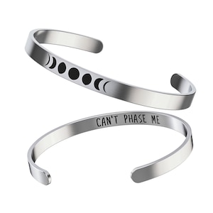 May include: Silver bangle bracelet with the text "CAN'T PHASE ME" and a moon phase design.