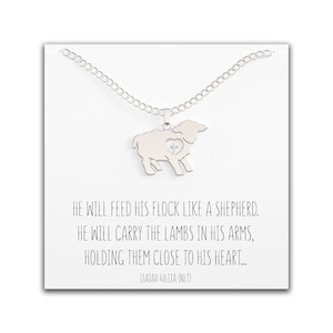 May include: A silver necklace with a pendant shaped like a lamb with a heart and cross inside. The necklace comes with a card that reads "He will feed his flock like a shepherd. He will carry the lambs in his arms, holding them close to his heart... Isaiah 40:11A (NLT)"