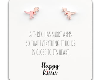 May include: A pair of pink T-Rex earrings with red hearts. The earrings come with a card that reads "A T-Rex has short arms so that everything it holds is close to its heart." The card also says "Happy Kisses" with a small red heart.