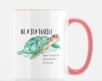 May include: White ceramic mug with a pink rim and handle. The mug features a watercolor illustration of a sea turtle with the text "Be a Sea Turtle" and "Happiest Floating At Sea And Comfortable In Your Own Shell."