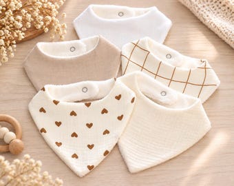 May include: A set of five triangular baby bibs featuring various designs including solid white, solid beige, a white bib with a brown grid pattern, a white bib with a brown heart print, and a plain cream bib, each with a metal snap closure.