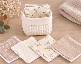 May include: A small, square, cream-colored waffle-weave fabric basket containing several square facial pads. The pads feature various patterns, including a beige floral print, a solid light brown, and a white floral design, all with white trim.