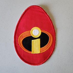 May include: Red fabric patch with an embroidered yellow and black "I" symbol, similar to the superhero character Mr. Incredible.