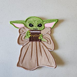 May include: A green and brown embroidered patch of a fictional character holding a book that says "MATH" on the cover.