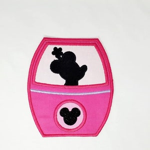 May include: Pink embroidered patch featuring a silhouette of Mickey Mouse in a pink vehicle with a Mickey Mouse head on the front.