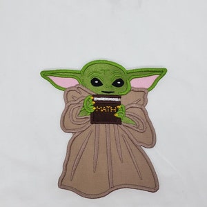 May include: Green and brown embroidered patch of a character from the Star Wars franchise holding a book that says "MATH" on the cover.