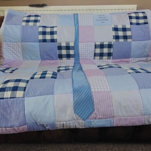 May include: A blue and white patchwork quilt with a blue tie sewn in the centre. The quilt has a handwritten note that says "Charlie, love with Dad & Family xx".