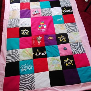 May include: A pink and white quilt with a variety of colourful squares. Each square has a different design, including a star, a zebra print, and a Disney logo. The quilt is made from a variety of fabrics, including cotton and flannel.