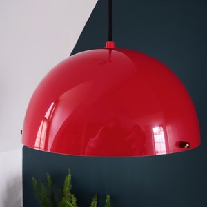 May include: A vibrant red pendant light with a curved, hemispherical shade. It is suspended by a black cable and a red fitting. The background features white, teal, and dark green sections.