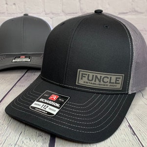 May include: Black and gray trucker hat with a gray mesh back. The hat has a black patch on the front that says "FUNCLE ESTABLISHED 2024". The hat is made by Richardson and is adjustable.