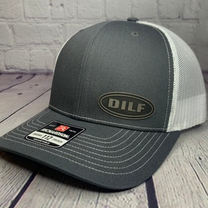 May include: A gray and white trucker hat with a black oval patch that says "DILF" on it. The hat is made by Richardson 112.