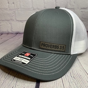 May include: A gray and white trucker hat with a black leather patch that says "Proverbs 3:5".