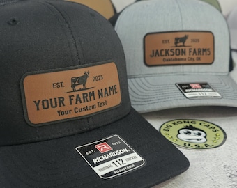 May include: Black trucker hat with a brown leather patch featuring the text "YOUR FARM NAME" and a cow graphic. The hat includes a Richardson 112 tag and is adjustable.