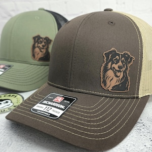 May include: Two adjustable Richardson 112 trucker hats. One is olive green with a black mesh back, the other is brown with a tan mesh back. Both have a leather patch of a dog. The hats have a curved brim.