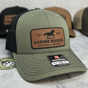 K&ouml;nnte beinhalten: Olivgr&uuml;ne Trucker-Kappe mit schwarzem Mesh-R&uuml;cken und einem braunen Lederpatch. Der Patch zeigt eine Pferdesilhouette und den Text "DIAMOND BOARDING" und "BOARDING & GROOMING". Die Kappe ist verstellbar.