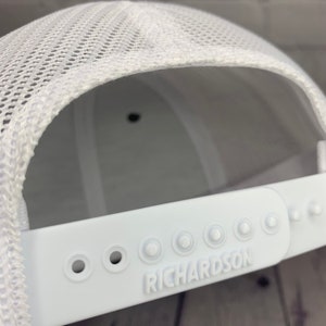 May include: White mesh trucker hat with a white adjustable strap and the word "RICHARDSON" embossed on the strap.