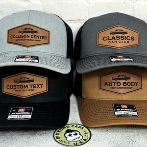 May include: Four trucker hats with a classic car logo on a brown leather patch. The hats are gray, black, and brown with black mesh backs. Text on the patches includes "Collison Center", "Classics Car Club", "Custom Text", and "Auto Body".