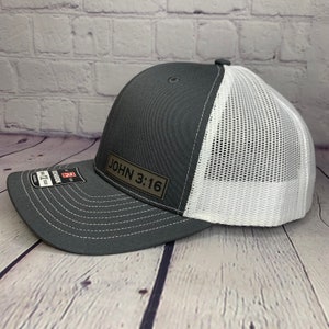 May include: A gray and white trucker hat with a black leather patch that says "JOHN 3:16".
