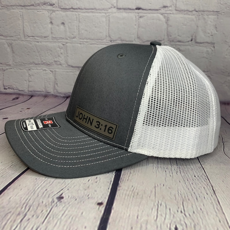 May include: A gray and white trucker hat with a black leather patch that says "JOHN 3:16".