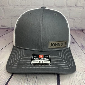 May include: A gray and white trucker hat with a brown patch that says "JOHN 3:16". The hat is adjustable and has a Richardson 112 logo.