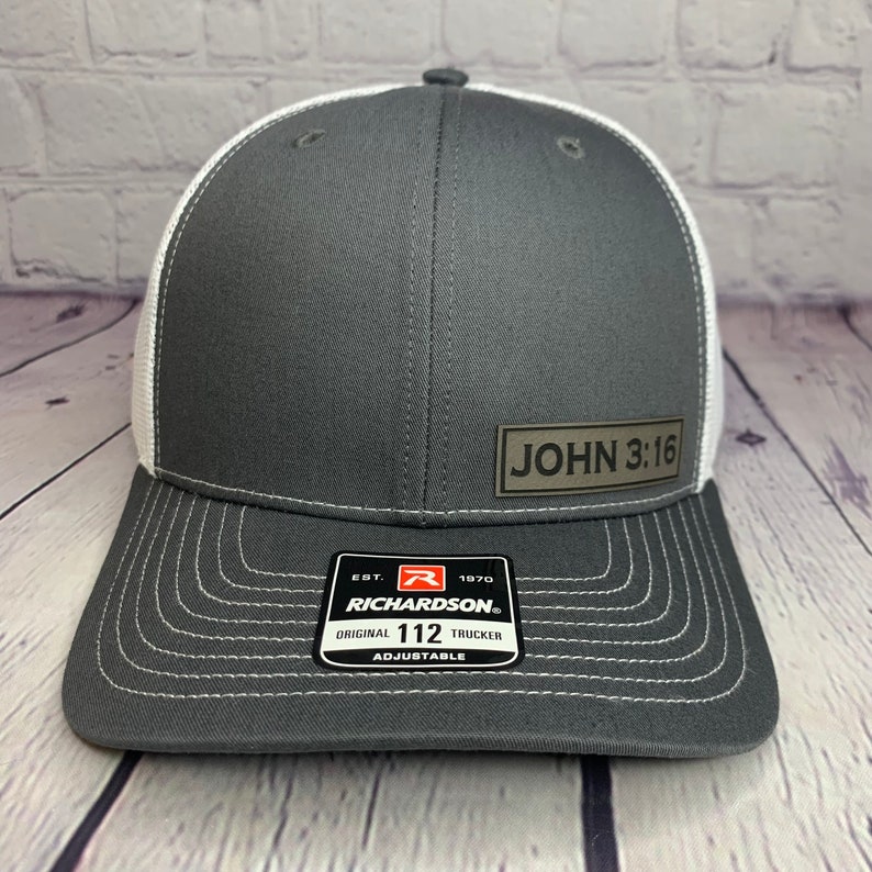 May include: A gray and white trucker hat with a brown patch that says "JOHN 3:16". The hat is adjustable and has a Richardson 112 logo.