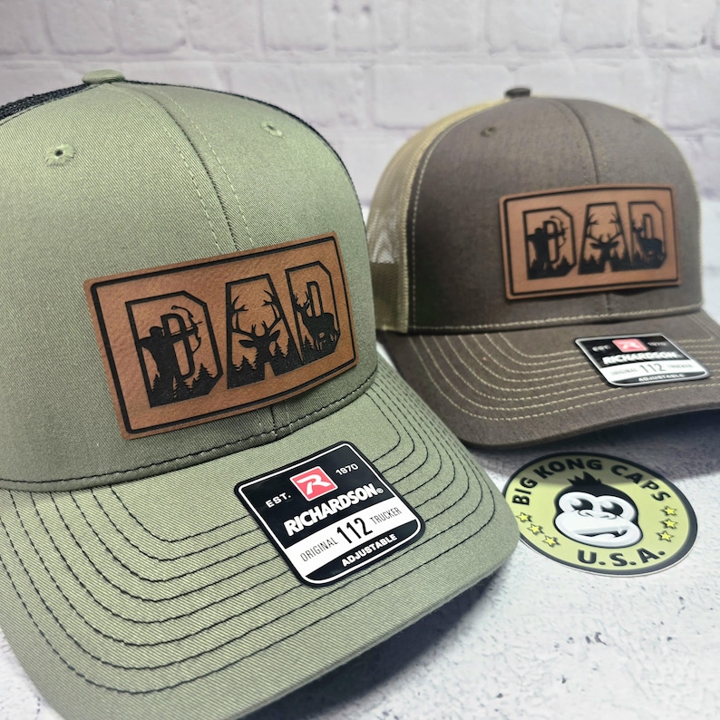 May include: Two trucker hats with leather patches that read "DAD" with hunting-themed graphics. One hat is olive green with a black mesh back, and the other is brown with a tan mesh back. Both have "RICHARDSON" tags.