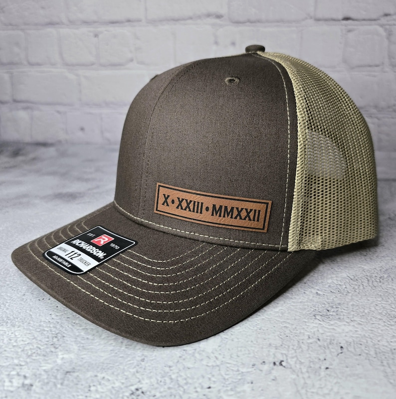 May include: A brown and beige trucker hat with a brown leather patch that says "X.XXIII.MMXXII".