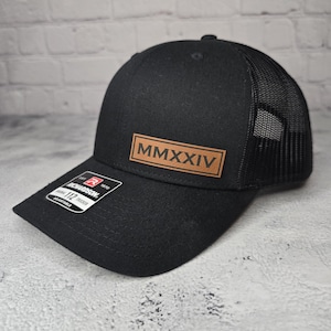 May include: Black trucker hat with a brown leather patch that says "MMXXIV" on the front.