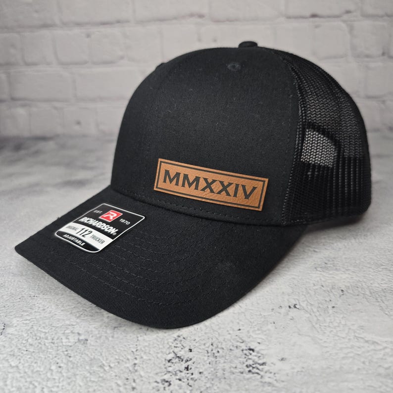 May include: Black trucker hat with a brown leather patch that says "MMXXIV" on the front.