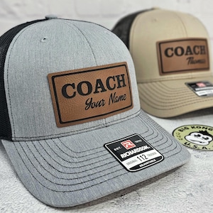 May include: Two trucker hats with a patch that says "COACH Your Name" and "COACH Thomas". The hats are gray and tan with black mesh backs. The gray hat has a Richardson 112 tag.