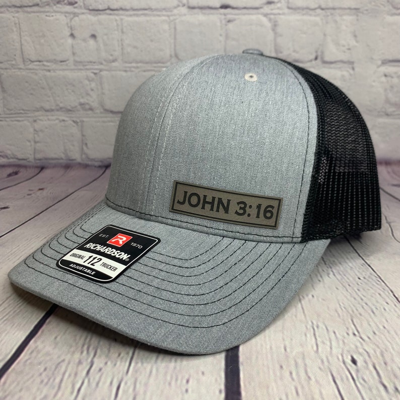 May include: A gray and black trucker hat with a brown leather patch that says "JOHN 3:16".