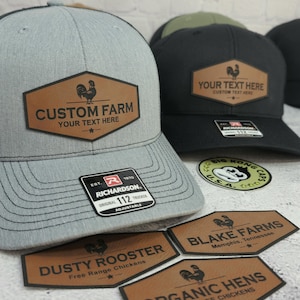 May include: Gray and black trucker hats with a brown leather patch featuring a rooster graphic and the text "CUSTOM FARM". The hats have a curved brim and adjustable strap. Additional patches with farm-related text are also visible.