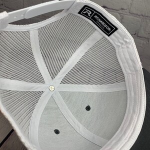 May include: White mesh trucker hat with a black brim and a white label with the text "Richardson" and a logo on the inside.