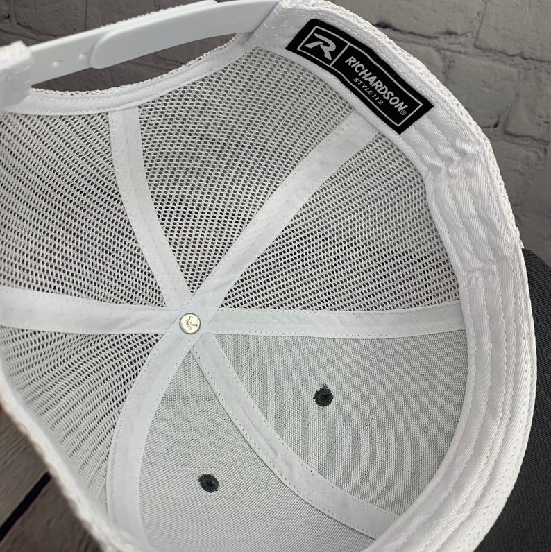 May include: White mesh trucker hat with a black brim and a white label with the text "Richardson" and a logo on the inside.