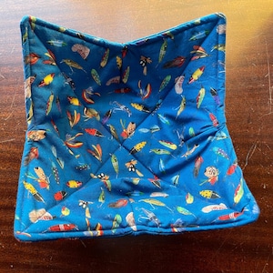 May include: A blue quilted bowl with a pattern of colorful fishing lures. The bowl is folded and ready to be used.